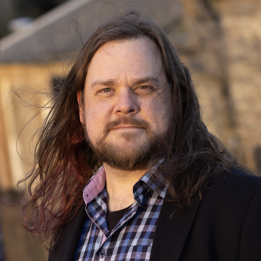 A outdoor portrait of Steve Ross wearing a casual button-up shirt and sport jacket